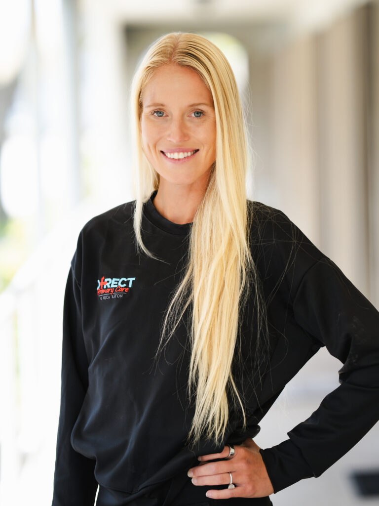 Smiling blonde woman wearing a black Direct Primary Care of Boca Raton shirt in a bright office.